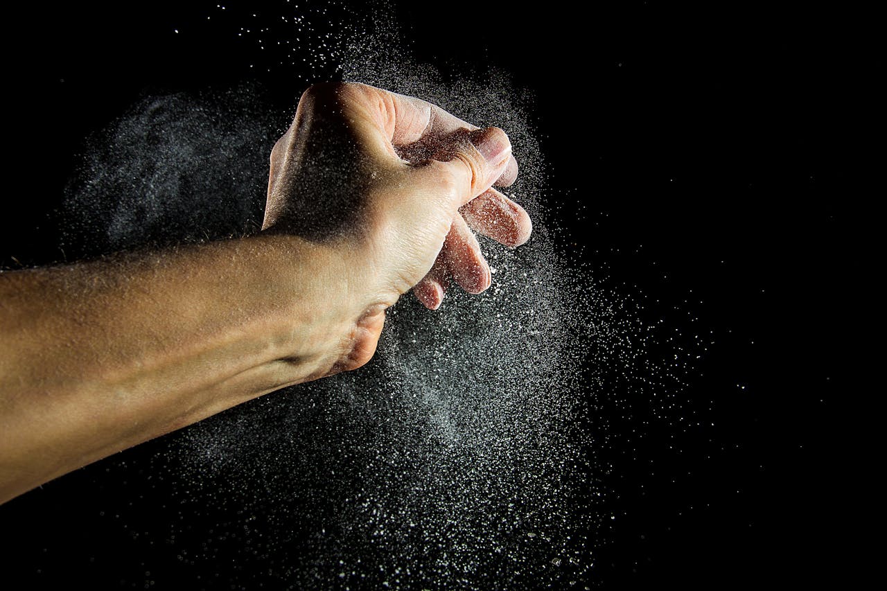 Close-up of a hand clapping with powder creating a dramatic effect against a black background.